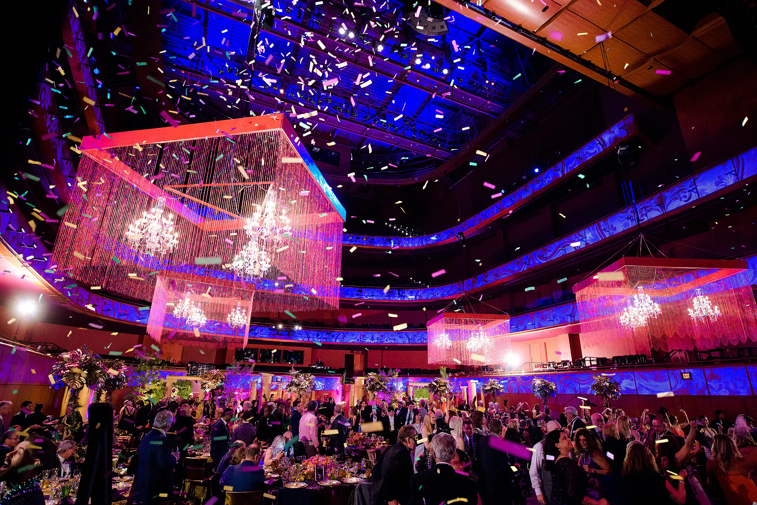 Brightly lit corporate event with chandelier lighting, colorful confetti, and elegant decorations.