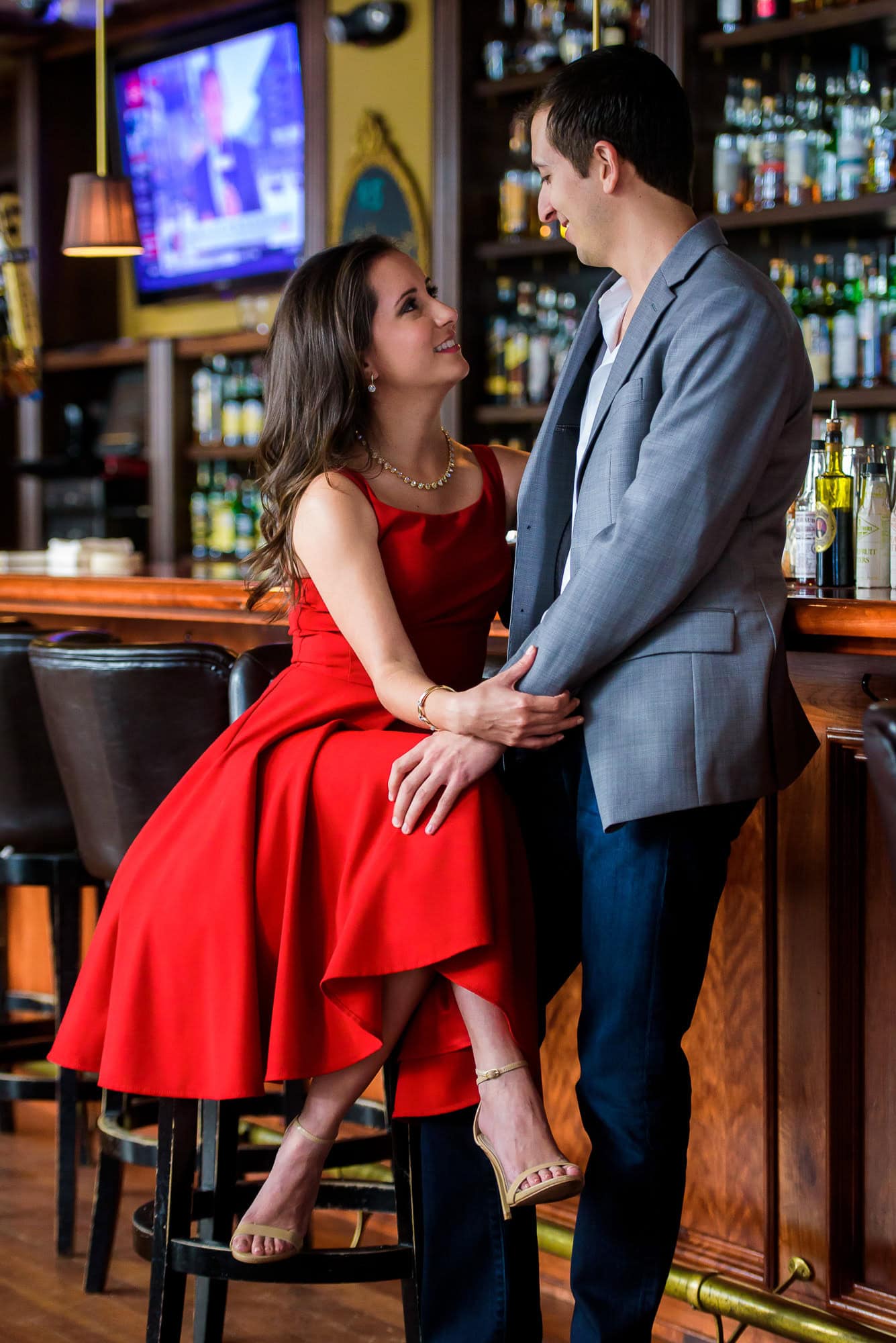 Vanessa & Matthew's Downtown San Antonio Engagement Session | Couple sharing a moment at the bar in Bohanan's, red tufted dress and gray suit